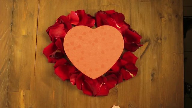 Girl lays out a heart on a wooden table from rose petals. Time laps