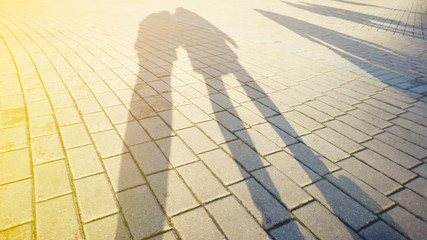 Shadows and silhouettes of people on paving stone at a city during sunset. Blank background