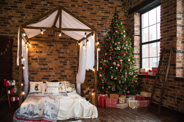 bed with canopy valance baldachin decorated with decorative pillows with a pattern and lamps . Christmas tree with gifts loft style brick wall. new year 2019 © Yulia
