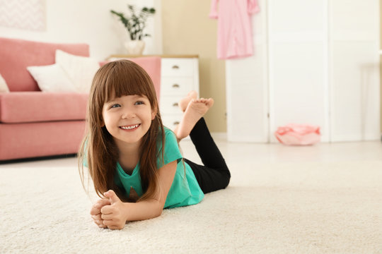 Cute little girl lying on carpet at home. Space for text
