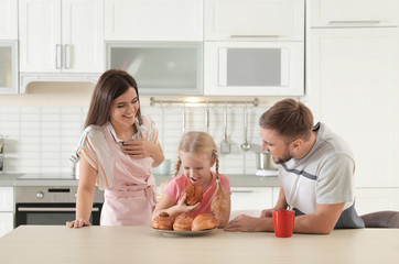 Happy couple treating their daughter with freshly oven baked bun in kitchen