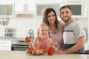 Happy family with freshly oven baked buns at table in kitchen. Space for text