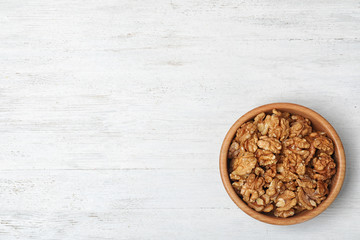 Fototapeta na wymiar Tasty walnuts in bowl and space for text on wooden background, top view