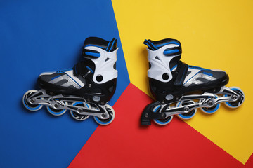 Pair of inline roller skates on color background, top view
