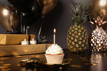 Cupcake with candle and blurred balloons on background