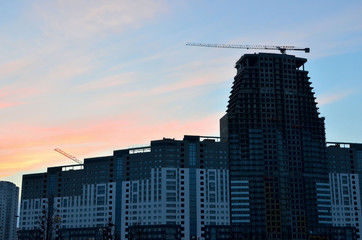 Fototapeta na wymiar Crane and building construction site against blue sky with blank white billboard for advertisement at the top of tower architecture. against the blue sky with the evening sunset