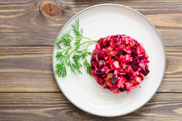 National Russian salad - vinaigrette - from boiled vegetables, sauerkraut and pickled cucumbers on a plate on a wooden table. Top view