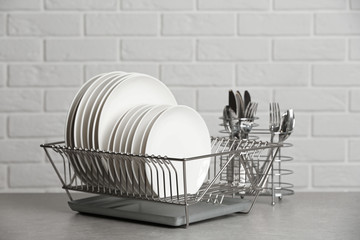 Dish rack with clean plates on table near brick wall
