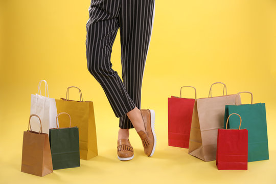 Young woman with shopping bags on color background, closeup of legs