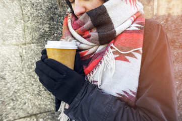 Young beautiful girl in gloves and in a large cozy scarf holding a paper cup of takeaway coffee. Coffee to go in winter concept