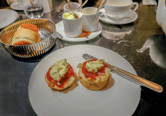 White plate with scone.  Jam and cream applied with a knife.