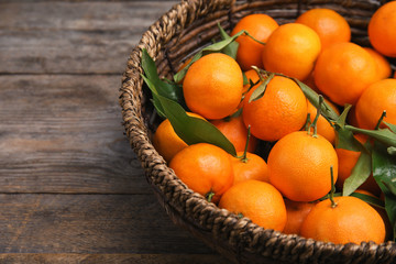 Fresh ripe tangerines in wicker basket on wooden table. Space for text