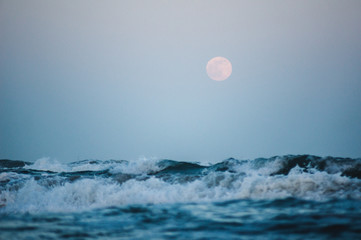 Splashing wave on the Black sea in the night with rising full moon in the background