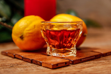 Small cup of brandy and lemon with candle. Wooden mat and wooden rustic table. Close-up.