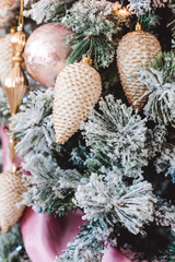 Christmas tree with beautiful winter decorations, pink ball, white cones, golden icicles, pink tape and snowflackes on the brunches. Closeup picture. Home interior. New Year holidays.