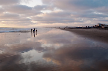 People standing in the shallow surf on a beach at sunset next to the Pacific ocean is southern California, USA