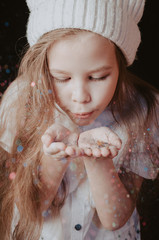 Little girl blowing on palm with sparkles