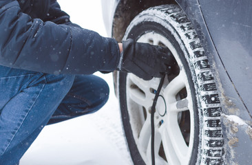 Driver is inflating a tire by car air compressor on the winter road.