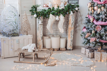 Christmas interior decorations: christmas tree with many balls, toys and pink tape, fireplace with big candles and woolen white socks, big clocks on the background, sled and white bear.