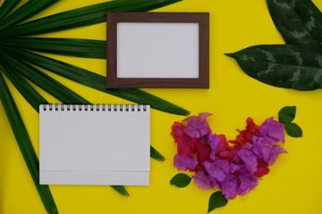 Mock-up white paper with space for text or picture on yellow background and tropical leaves and flowers.