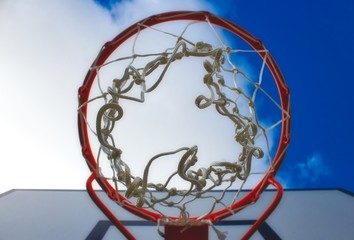 Closeup up basketball hoop looking up from below against a blue cloudy sky