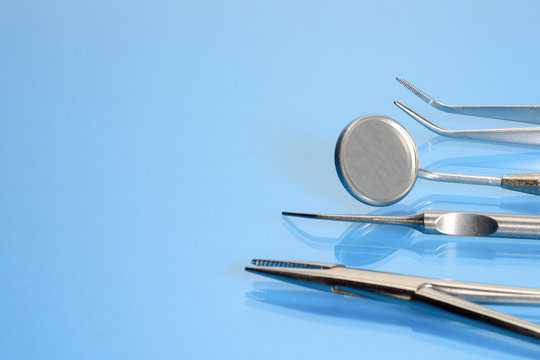 Dentist tools: mirror, explorer, tweezers and forceps or kornzange on blue glass background with copy space.