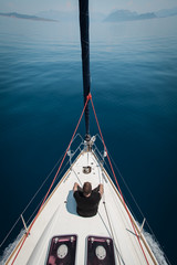 On the nose of a sailing yacht sits a man and looks at the water.