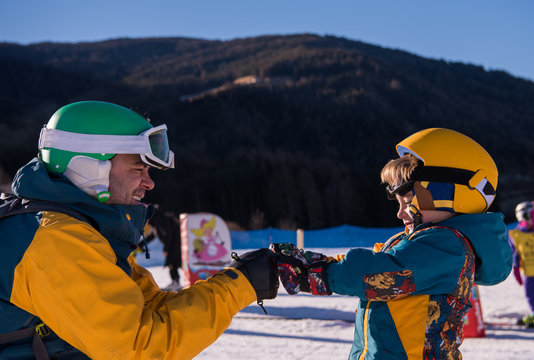 father preparing his little son for the first time on a snowboard