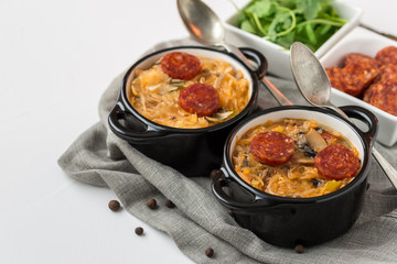 Slovak Christmas national cabbage soup in two small black pots with sausage on the tablecloth background.v