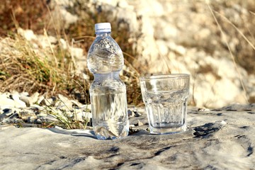 Una botella de agua mineral,con vaso sobre una roca