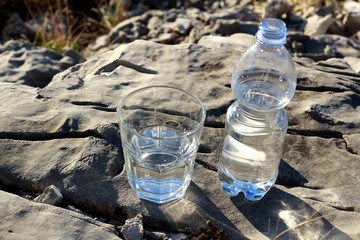 Una botella de agua mineral,con vaso sobre una roca