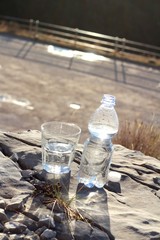 Una botella de agua mineral,con vaso sobre una roca