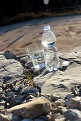 Una botella de agua mineral,con vaso sobre una roca
