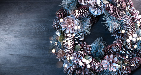 Christmas holiday background. Xmas wreath with spruce, cones and lights. Christmas decoration border over wooden table. Tabletop. Flatlay