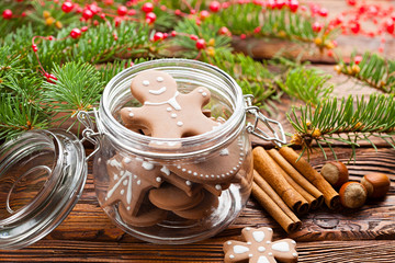 Gingerbread Christmas cookies in a jar, cinnamon, hazelnuts and branch of spruce tree on wooden table
