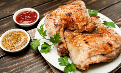 Chicken legs in a plate with mustard and ketchup on a wooden background.