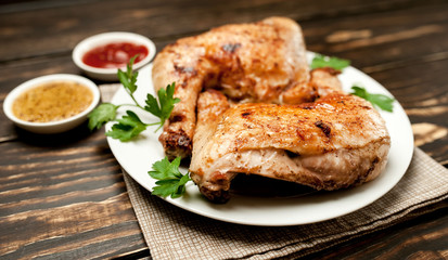 Chicken legs in a plate with mustard and ketchup on a wooden background.