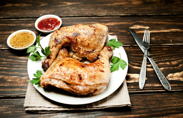 Chicken legs in a plate with mustard and ketchup on a wooden background.