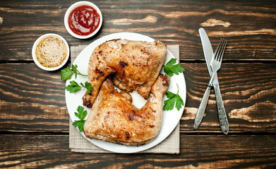 Chicken legs in a plate with mustard and ketchup on a wooden background.