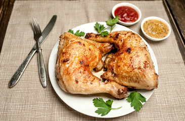 Chicken legs in a plate with mustard and ketchup on a wooden background.