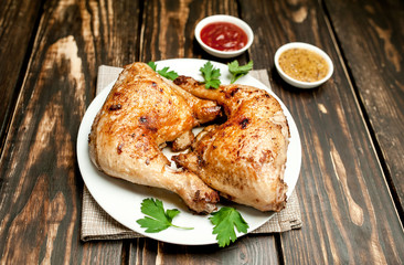 Chicken legs in a plate with mustard and ketchup on a wooden background.