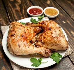 Chicken legs in a plate with mustard and ketchup on a wooden background.