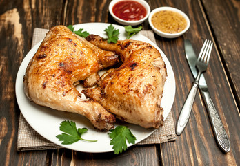 Chicken legs in a plate with mustard and ketchup on a wooden background.