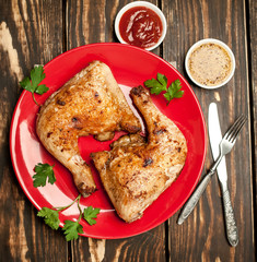 Chicken legs in a plate with mustard and ketchup on a wooden background.