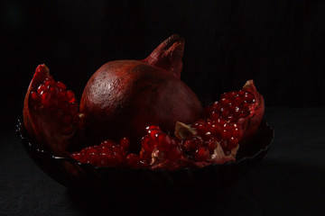 Appetizing red pomegranate in a plate on a dark background