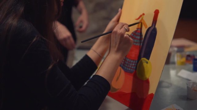 Young woman artist is painting picture on canvas in art studio. Slowmotion shot