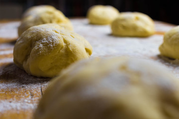 Hefeteig f&uuml;r Dampfnudeln, Rohlinge liegen auf einem Holzbrett mit Mehl best&auml;ubt