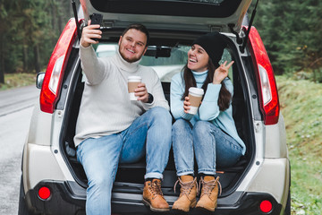 man and woman stop to drink warm up tea and taking selfie in car