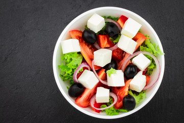 Greek salad with fresh vegetables, feta cheese and black olives on a dark background. Top view