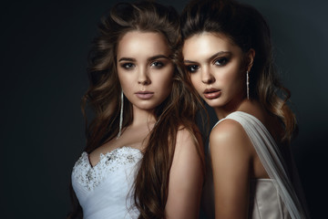 Close up portrait of two beautiful models with perfect take up and hairstyle wearing wedding dresses and luxurious earrings. Isolated on dark grey background. Studio shot © obrik